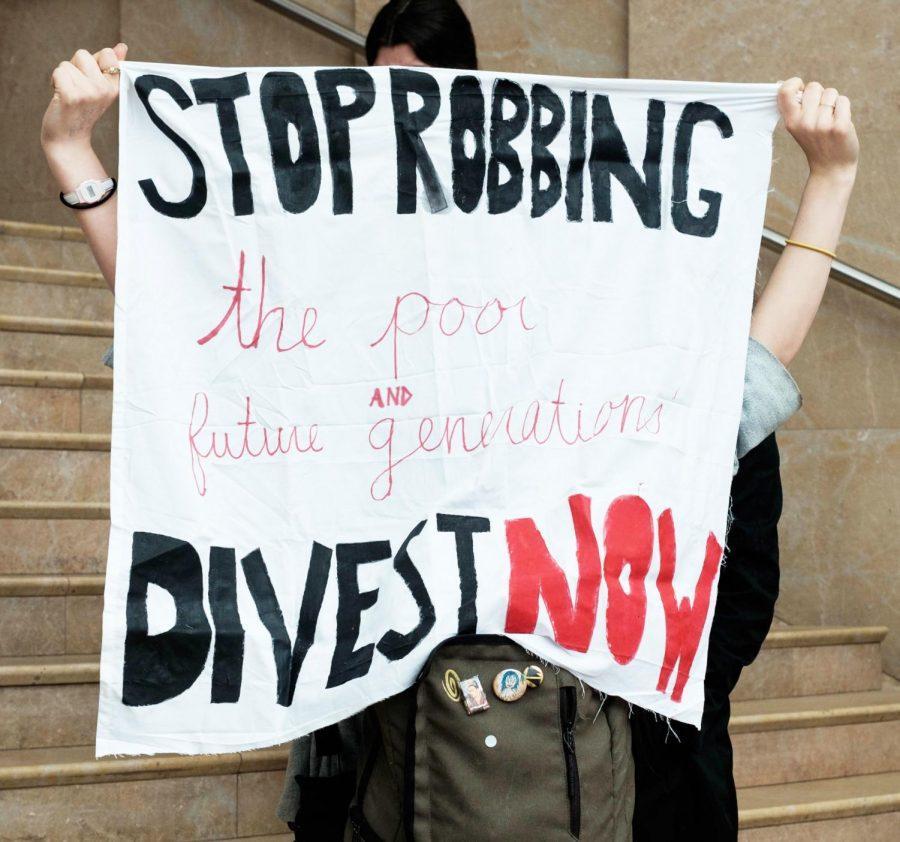 A+demonstrator+holds+a+banner+that+demands+NYU+to+terminate+all+investments+in+fossil+fuel+companies.