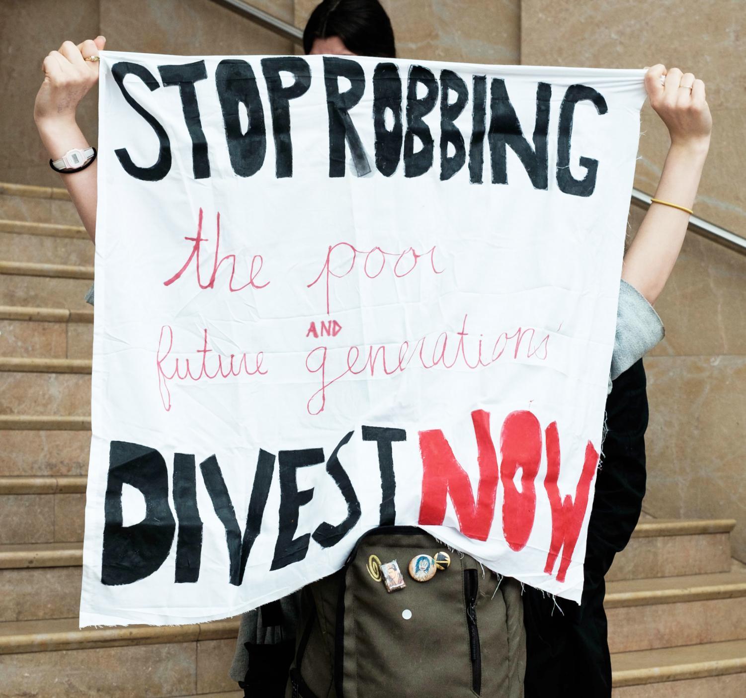 A demonstrator holds a banner that demands NYU to terminate all investments in fossil fuel companies.