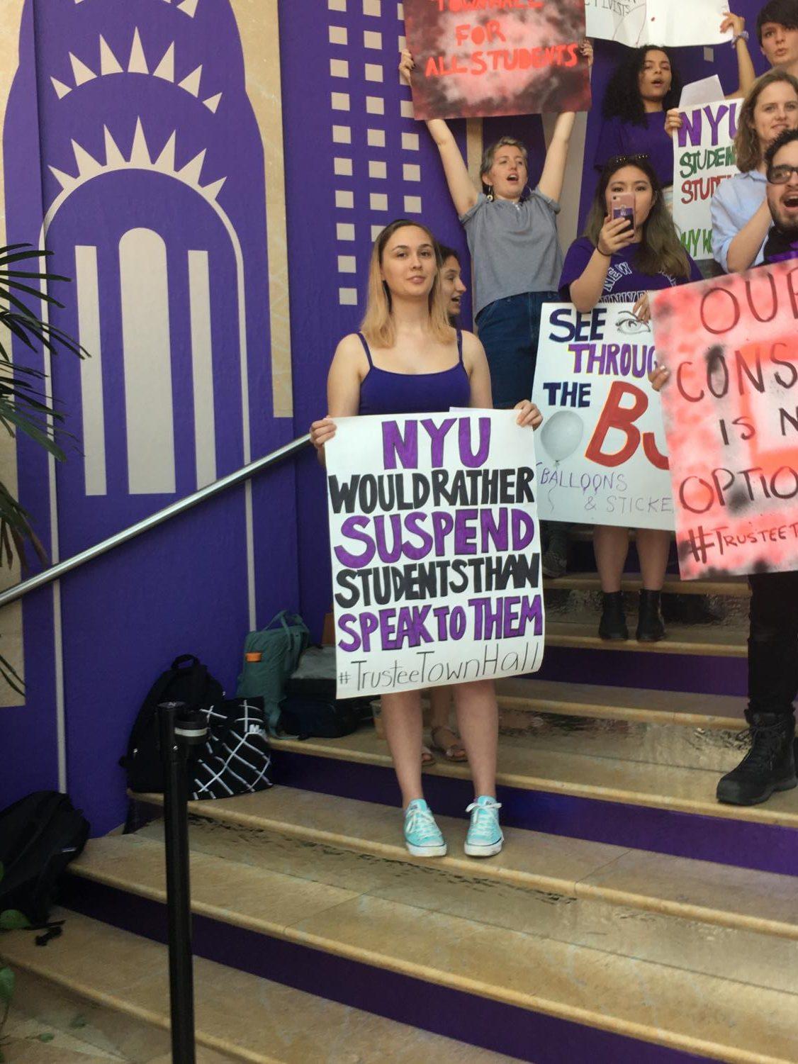 On the steps inside the Kimmel Center for University Life, a student activist holds a sign that reads,