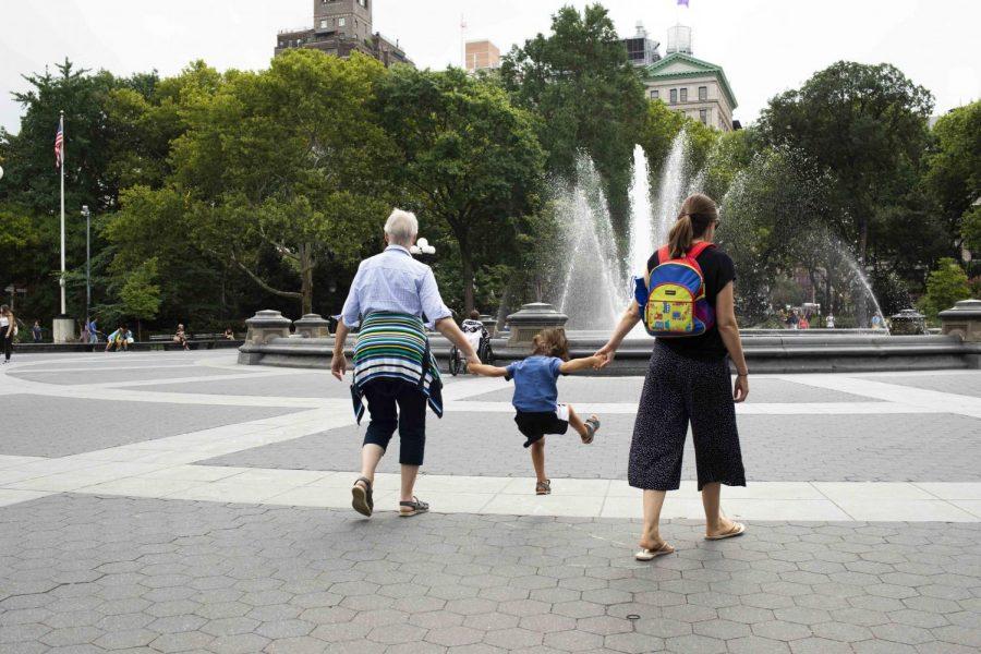 A+boy+jumps+while+holding+his+two+guardians%27+hands+in+Washington+Square+Park+on+a+late+summer+morning.